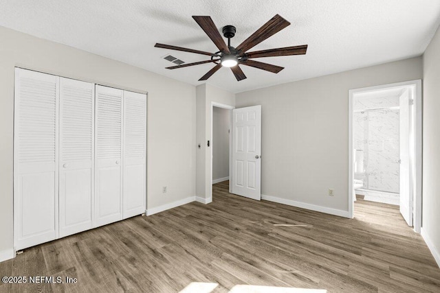 unfurnished bedroom with connected bathroom, a closet, wood-type flooring, and a textured ceiling