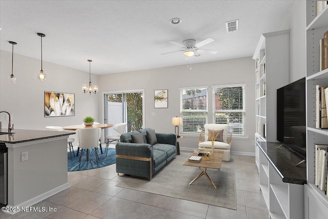 living room featuring a textured ceiling, sink, light tile patterned floors, and ceiling fan with notable chandelier