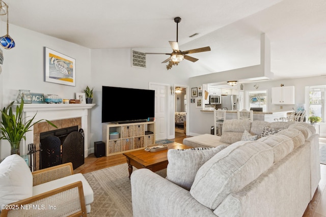 living room featuring a tile fireplace, ceiling fan, and light hardwood / wood-style floors