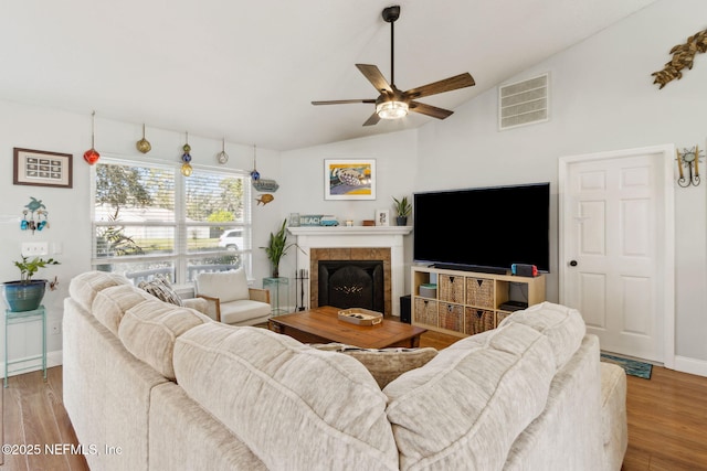 living room featuring a tile fireplace, vaulted ceiling, light hardwood / wood-style flooring, and ceiling fan