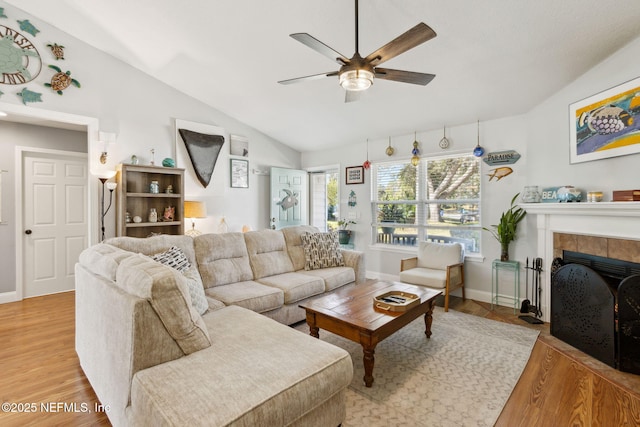 living room featuring a tile fireplace, light wood-type flooring, vaulted ceiling, and ceiling fan