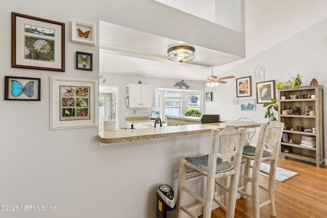 kitchen with ceiling fan, light wood-type flooring, white cabinetry, and kitchen peninsula