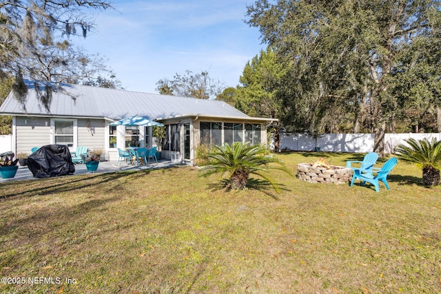 rear view of property featuring a patio, a fire pit, a lawn, and a sunroom