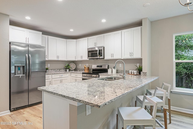 kitchen with sink, white cabinetry, appliances with stainless steel finishes, light hardwood / wood-style floors, and kitchen peninsula