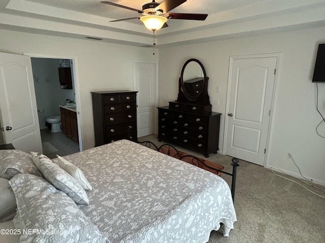 bedroom featuring ceiling fan, a raised ceiling, light carpet, and connected bathroom