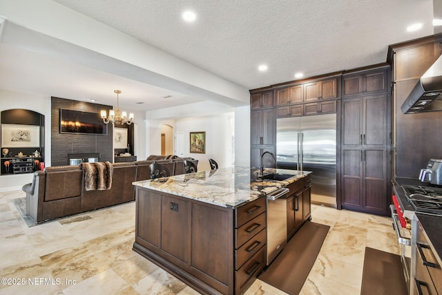 kitchen featuring a center island with sink, sink, a large fireplace, light stone counters, and stainless steel appliances