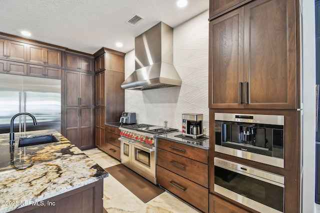 kitchen with high end appliances, sink, wall chimney exhaust hood, a textured ceiling, and light stone counters