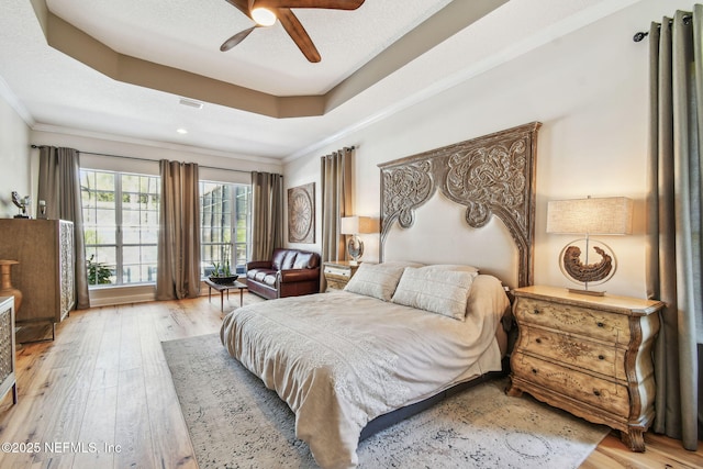 bedroom with a raised ceiling, ceiling fan, light wood-type flooring, a textured ceiling, and ornamental molding