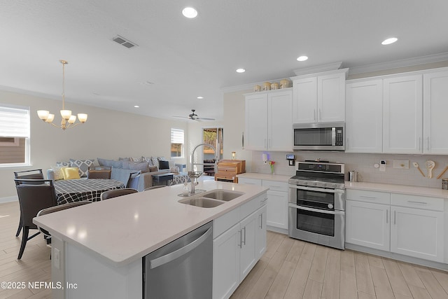 kitchen featuring appliances with stainless steel finishes, sink, white cabinets, hanging light fixtures, and a center island with sink