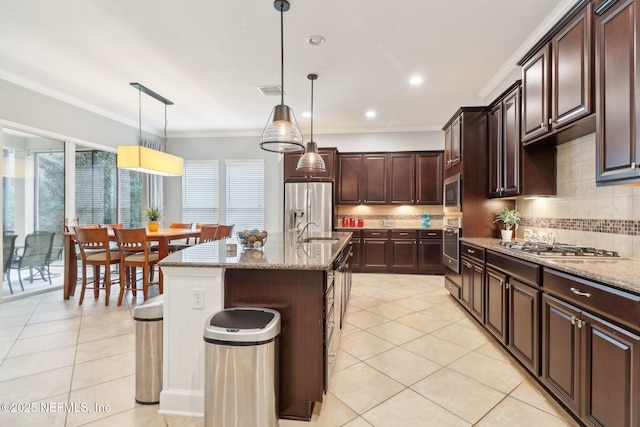 kitchen featuring stainless steel appliances, pendant lighting, tasteful backsplash, and an island with sink