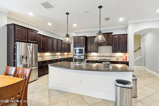 kitchen with decorative light fixtures, dark brown cabinetry, a kitchen island with sink, stainless steel appliances, and light tile patterned floors