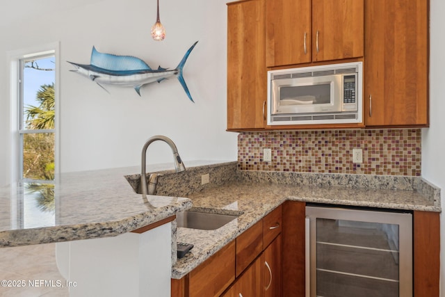 kitchen featuring stainless steel microwave, kitchen peninsula, pendant lighting, light stone counters, and wine cooler