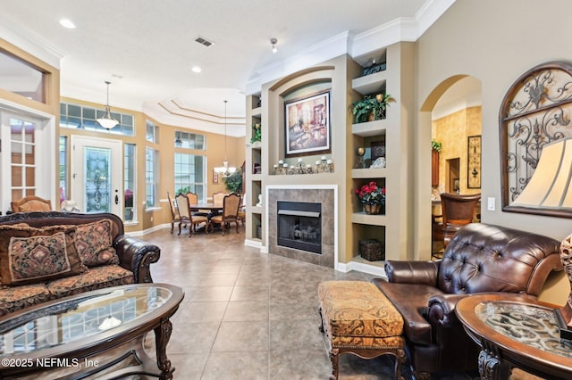 living room with light tile patterned floors, ornamental molding, built in features, a notable chandelier, and a fireplace