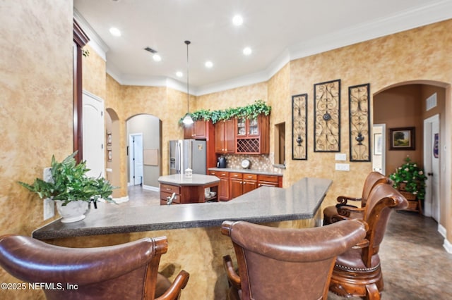 kitchen with stainless steel fridge with ice dispenser, backsplash, a kitchen breakfast bar, and kitchen peninsula