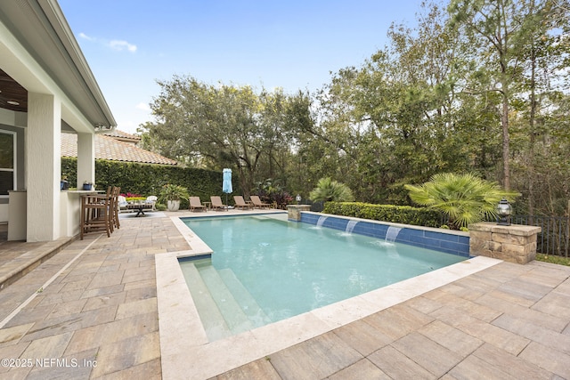 view of pool with an outdoor bar, pool water feature, and a patio area