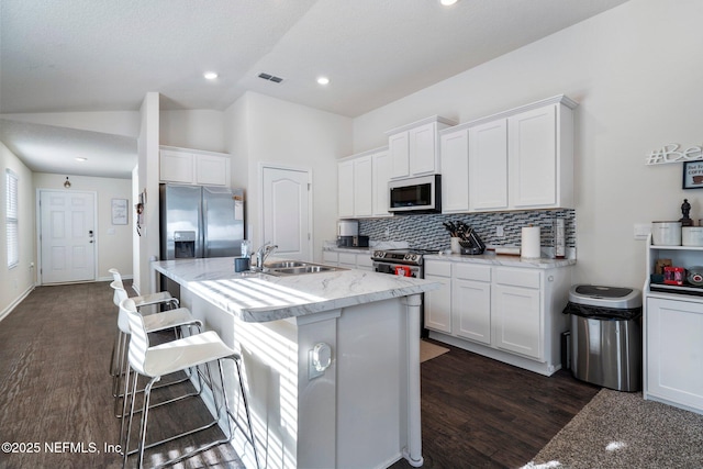 kitchen with stainless steel appliances, an island with sink, white cabinets, and a kitchen bar