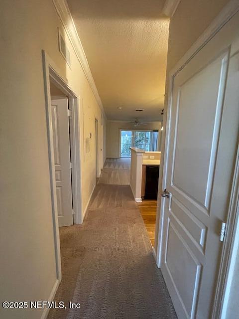 corridor with light carpet, a textured ceiling, and ornamental molding