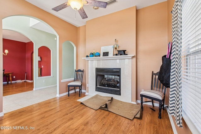 sitting room featuring ceiling fan, a tiled fireplace, and light wood-type flooring