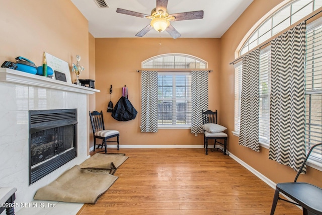 living area with a tile fireplace, ceiling fan, and light wood-type flooring