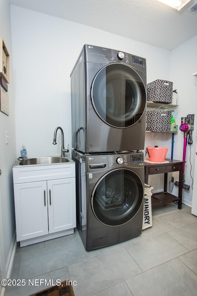 laundry room featuring cabinets, light tile patterned floors, stacked washer and clothes dryer, and sink