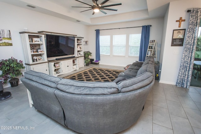 tiled living room with ceiling fan and a tray ceiling