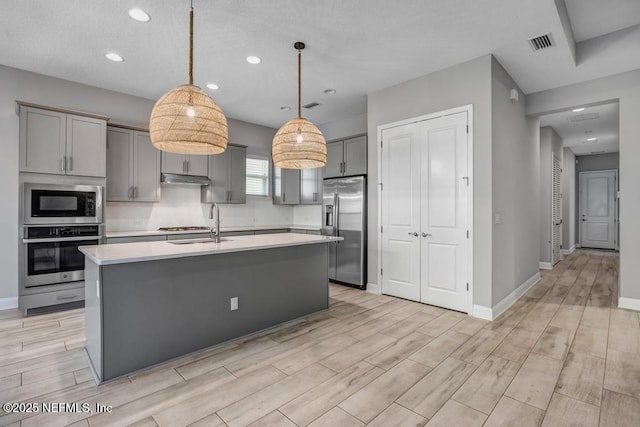 kitchen featuring stainless steel appliances, an island with sink, hanging light fixtures, and gray cabinetry