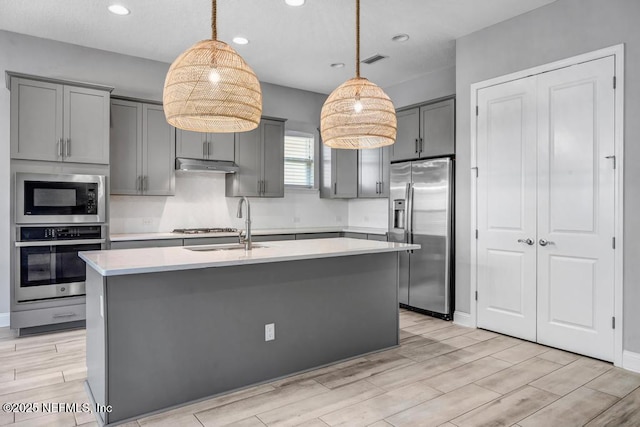 kitchen featuring pendant lighting, appliances with stainless steel finishes, a center island with sink, and gray cabinetry