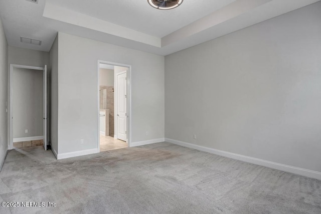 unfurnished bedroom featuring light carpet, a tray ceiling, and ensuite bath