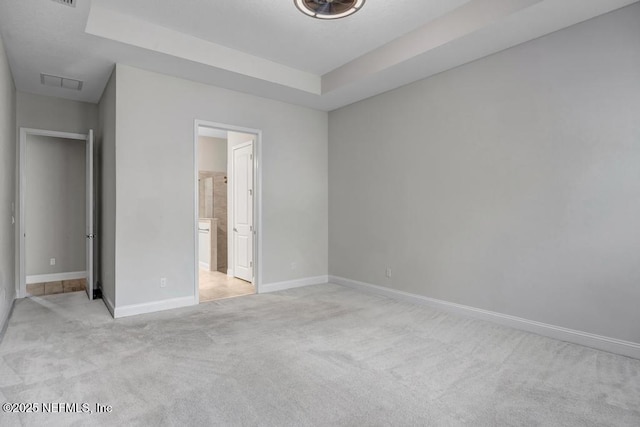 unfurnished bedroom with ensuite bathroom, a raised ceiling, and light carpet