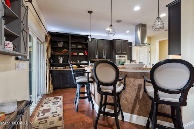 kitchen featuring a kitchen breakfast bar, island range hood, stainless steel oven, and hanging light fixtures