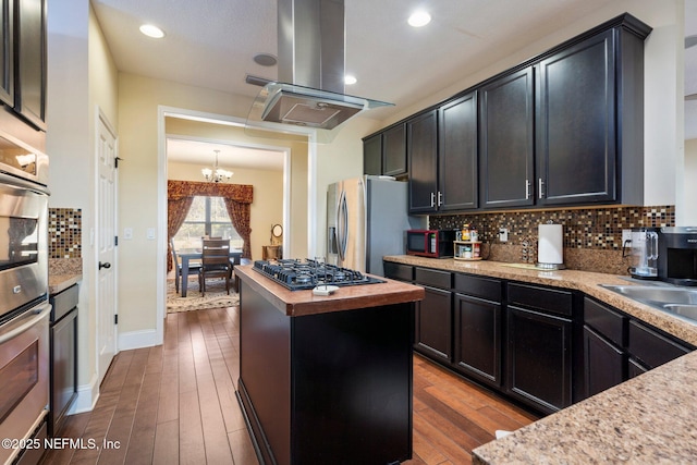 kitchen featuring dark wood-type flooring, an inviting chandelier, appliances with stainless steel finishes, a kitchen island, and island exhaust hood