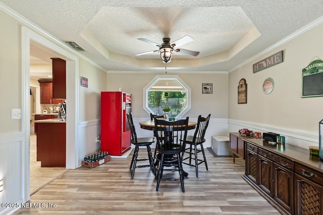 dining space with a tray ceiling, light hardwood / wood-style flooring, and a textured ceiling