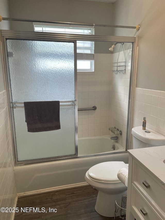 full bathroom with hardwood / wood-style floors, vanity, shower / bath combination with glass door, toilet, and tile walls