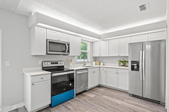 kitchen with a textured ceiling, stainless steel appliances, sink, white cabinets, and light hardwood / wood-style floors