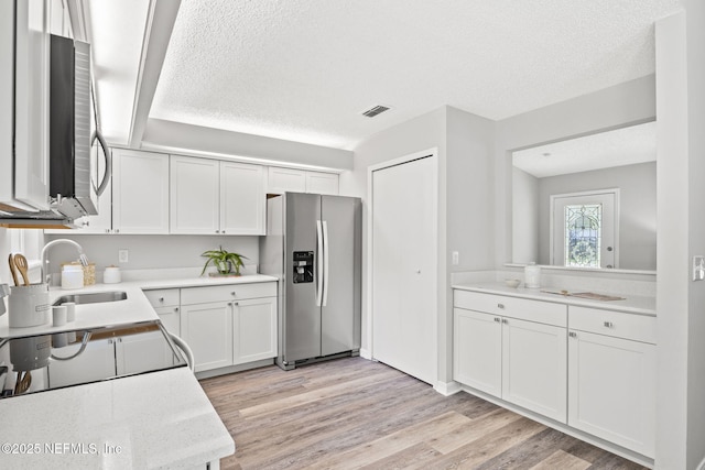 kitchen featuring a textured ceiling, sink, light hardwood / wood-style flooring, white cabinets, and stainless steel fridge with ice dispenser