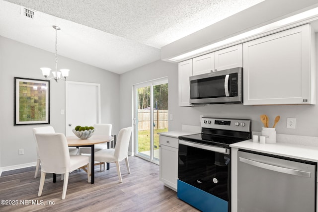 kitchen with decorative light fixtures, vaulted ceiling, stainless steel appliances, and white cabinetry