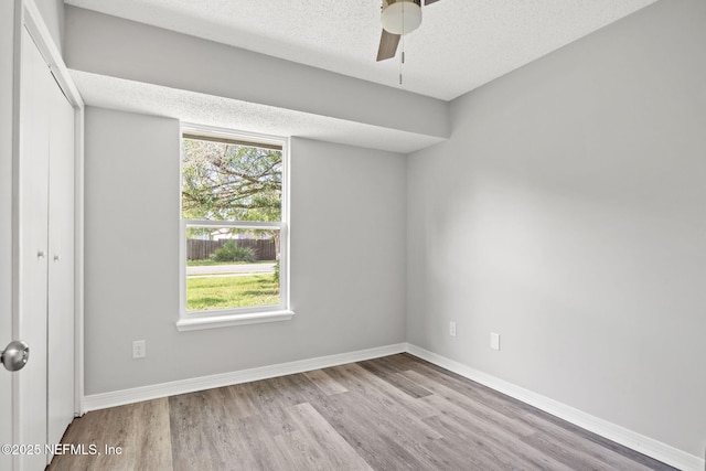 empty room featuring ceiling fan, light wood-type flooring, a textured ceiling, and a wealth of natural light