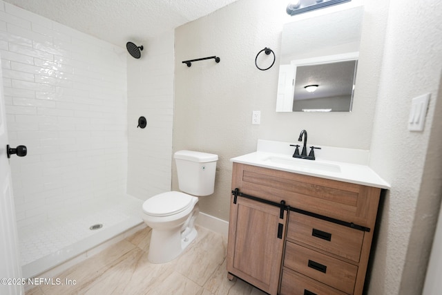 bathroom featuring tiled shower, a textured ceiling, vanity, and toilet