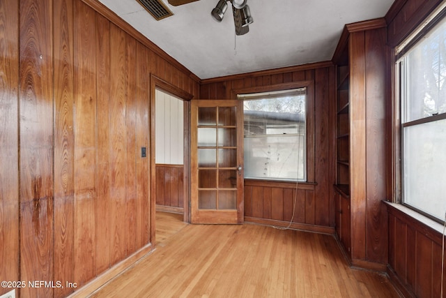 spare room featuring ceiling fan, french doors, crown molding, light hardwood / wood-style floors, and wooden walls