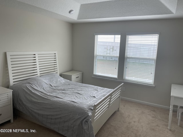 bedroom featuring multiple windows, a textured ceiling, a tray ceiling, and light carpet