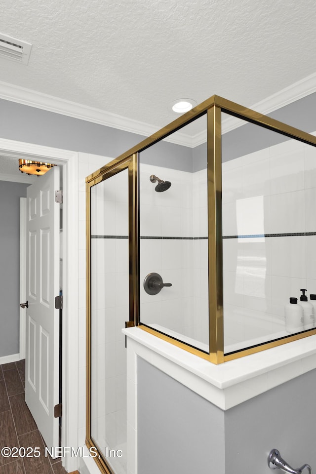 bathroom with a textured ceiling, a shower with shower door, and ornamental molding