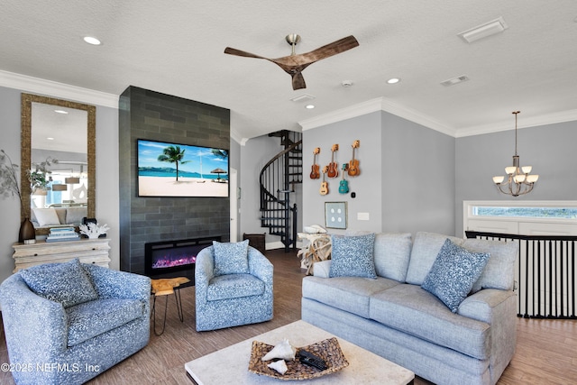 living room featuring a large fireplace, ornamental molding, hardwood / wood-style flooring, a textured ceiling, and ceiling fan with notable chandelier