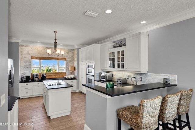 kitchen featuring white cabinets, kitchen peninsula, pendant lighting, a notable chandelier, and appliances with stainless steel finishes