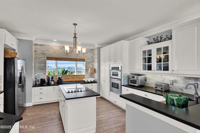 kitchen with appliances with stainless steel finishes, hanging light fixtures, a kitchen island, white cabinets, and sink