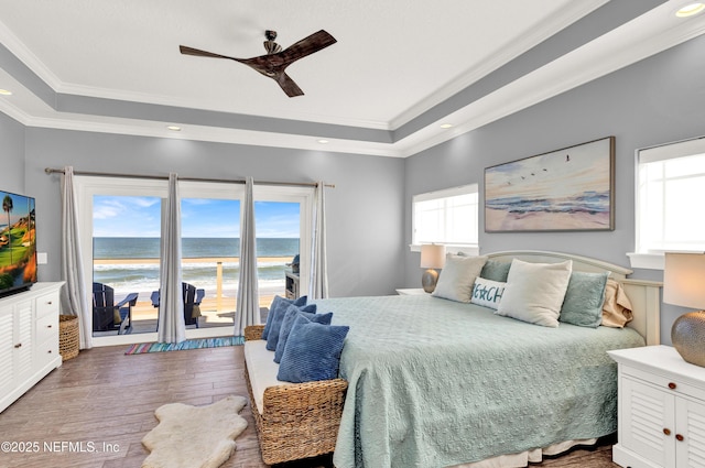 bedroom with a raised ceiling, a water view, ceiling fan, dark wood-type flooring, and access to outside