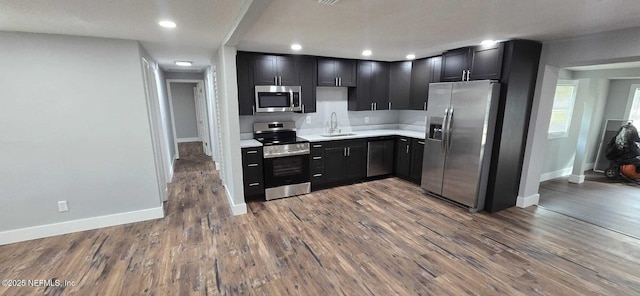 kitchen featuring stainless steel appliances, light countertops, wood finished floors, dark cabinetry, and baseboards