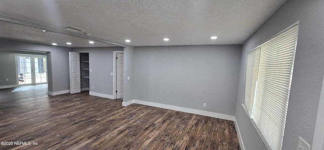 basement featuring dark wood-style floors, visible vents, a textured ceiling, and baseboards