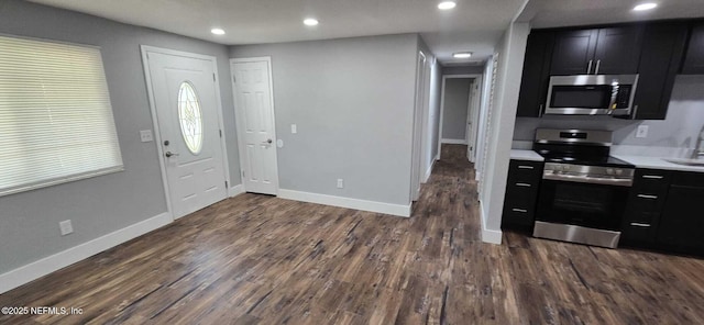 kitchen featuring dark wood-style flooring, light countertops, appliances with stainless steel finishes, dark cabinetry, and baseboards