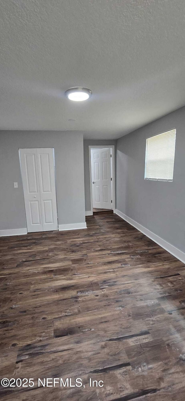 empty room featuring dark wood finished floors, a textured ceiling, and baseboards