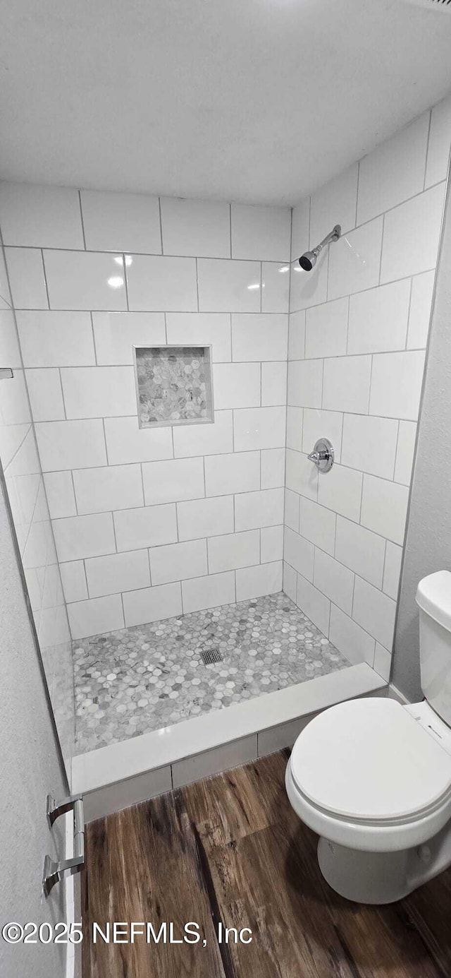 bathroom with toilet, tiled shower, and wood finished floors